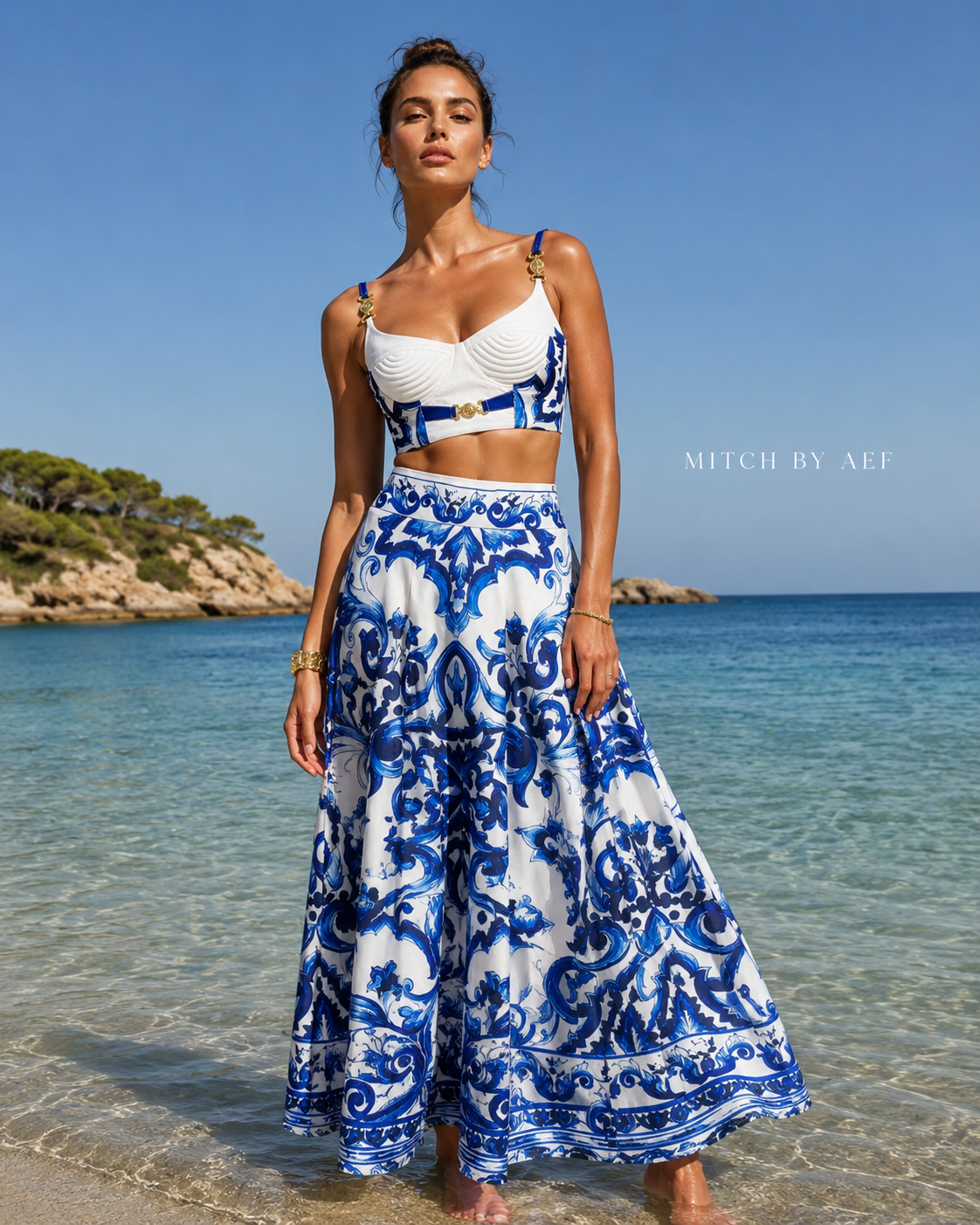Mannequin portant l’ensemble SANTORINI bleu et blanc face à la mer, photographié en contre-plongée sur une plage ensoleillée.
