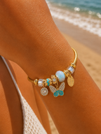 Bracelet jonc talisman doré charmes papillon turquoise opale et strass, porté bord de mer lumière dorée
