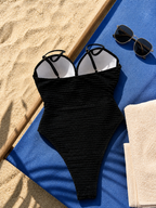 Maillot une pièce côtelé noir posé à plat sur serviette de plage bleue avec lunettes de soleil
