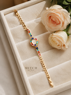 Montre bijou ÉCLAT dorée Arc-en-Ciel Joaillerie posée sur un écrin en velours ivoire avec des roses crème, cadran à strass multicolores et bracelet fin en alliage doré, idée cadeau femme MITCH By AEF
