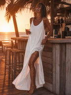 Robe longue blanche fluide bretelles fines, femme bronzée qui rit verre de rosé, bar de plage coucher de soleil