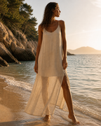 Robe maxi fluide crème bretelles fines, femme bronzée cheveux bouclés de face plage golden hour mer bleue