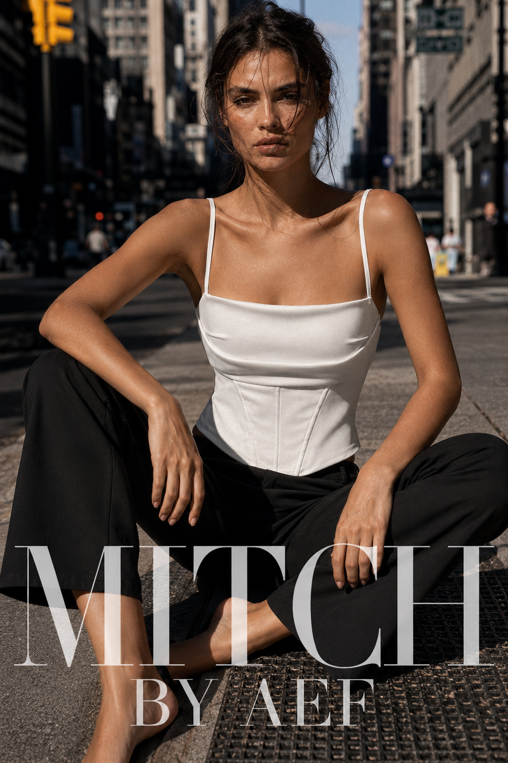 Femme assise dans une rue de New York portant un top corset blanc à fines bretelles et un pantalon noir.